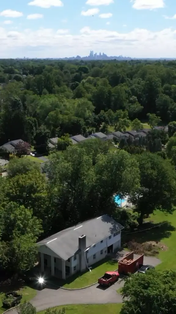 High drone view of the house among mature trees with the Center City Philadelphia skyline on the horizon.