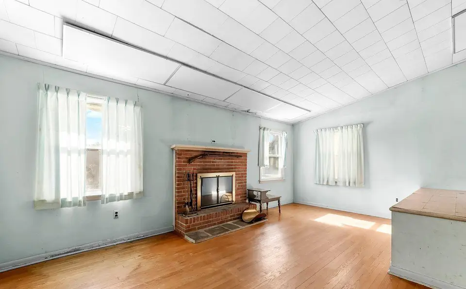 Before: the living room with a brick fireplace, tiled ceiling and older hardwood.