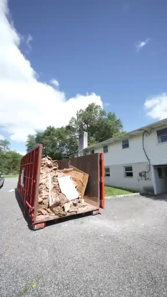 A full dumpster of demolition debris in the driveway beside the house.