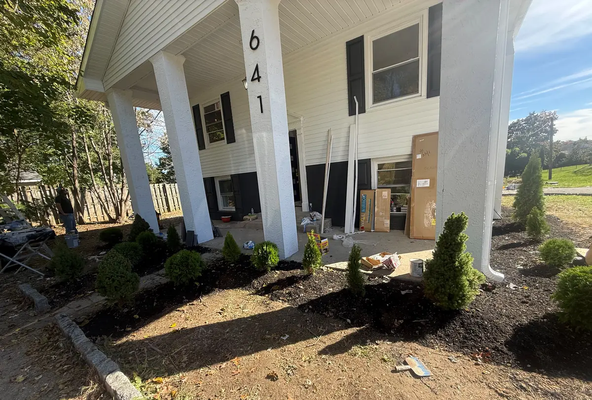 The front porch in October 2026 with the house number 641 on a white column and new evergreen plantings in fresh mulch beds.