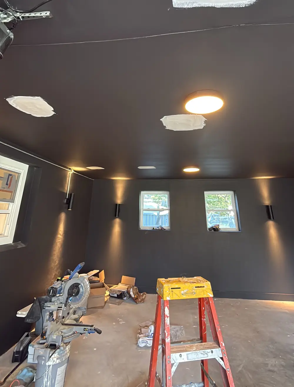 The garage with matte black walls and ceiling, custom showcase lighting from wall sconces and recessed lights, before the epoxy floor.