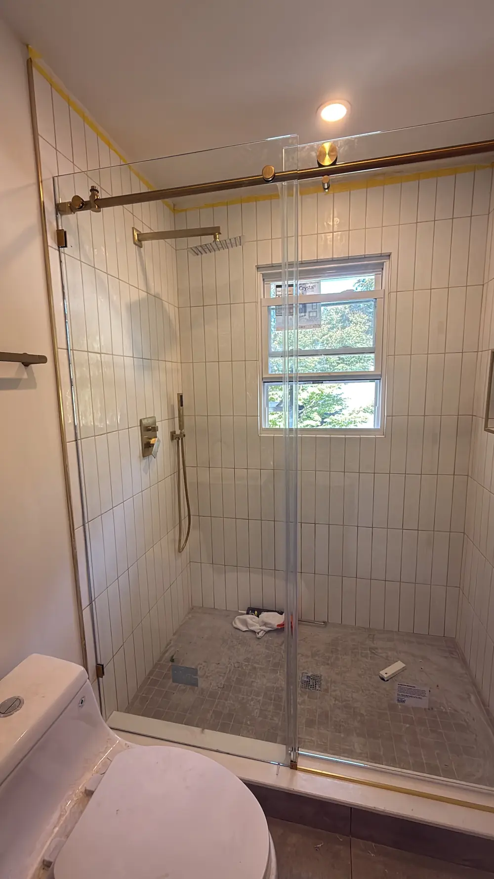 The bedroom 2 shower with stacked white tile, a brushed-gold rain head and a sliding glass door.
