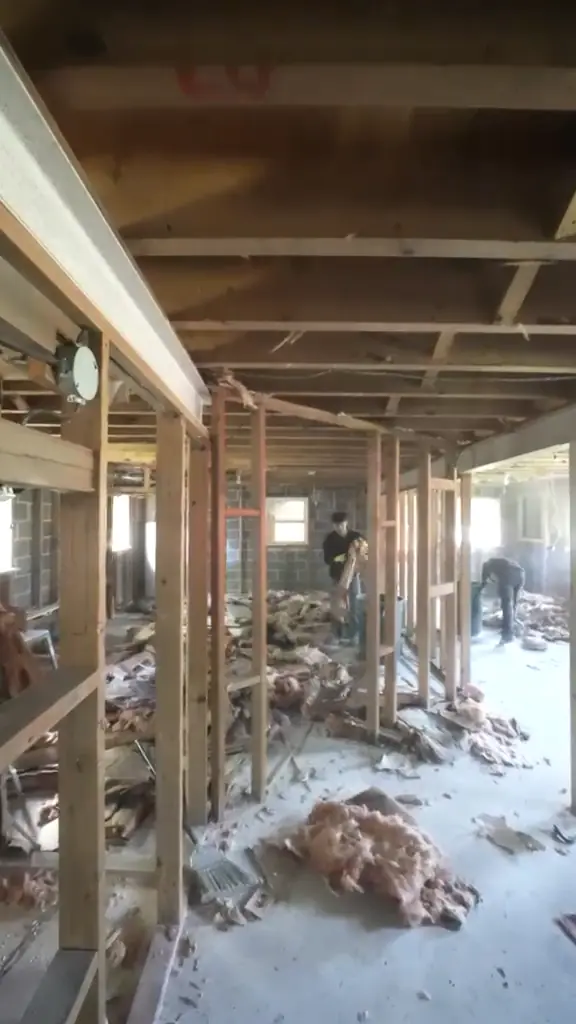 The old enclosed porch stripped to its framing, ceiling joists exposed and debris on the floor.